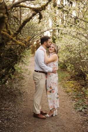 Couple shares tender moments along a nature trail with flowering trees creating a magical spring backdrop.