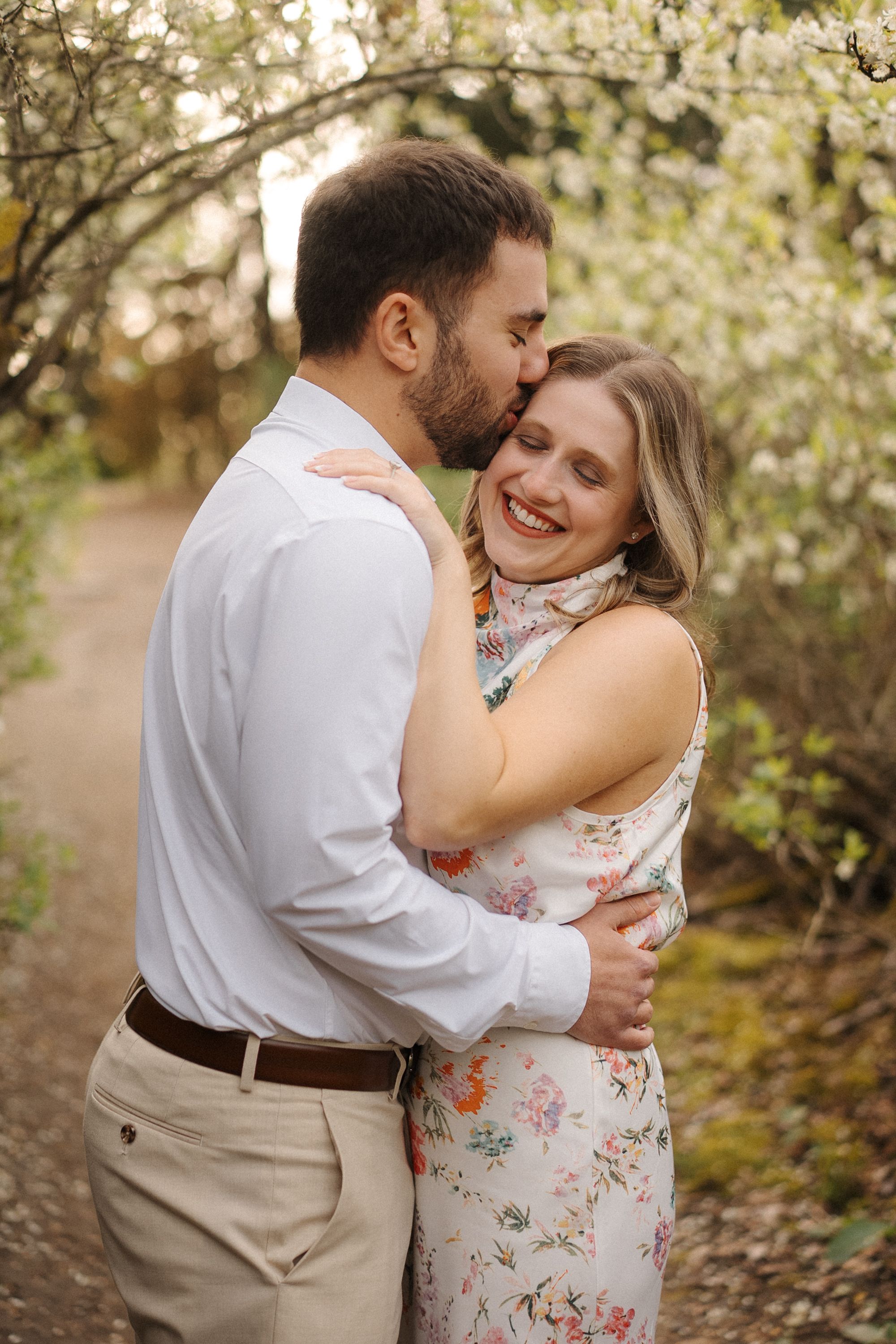 A couple shares romantic moments among blooming spring trees in a natural outdoor setting.