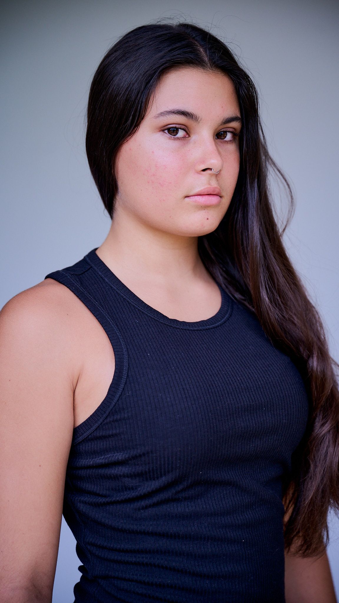 Model in white crop top and baggy blue jeans poses on black stool against light background.