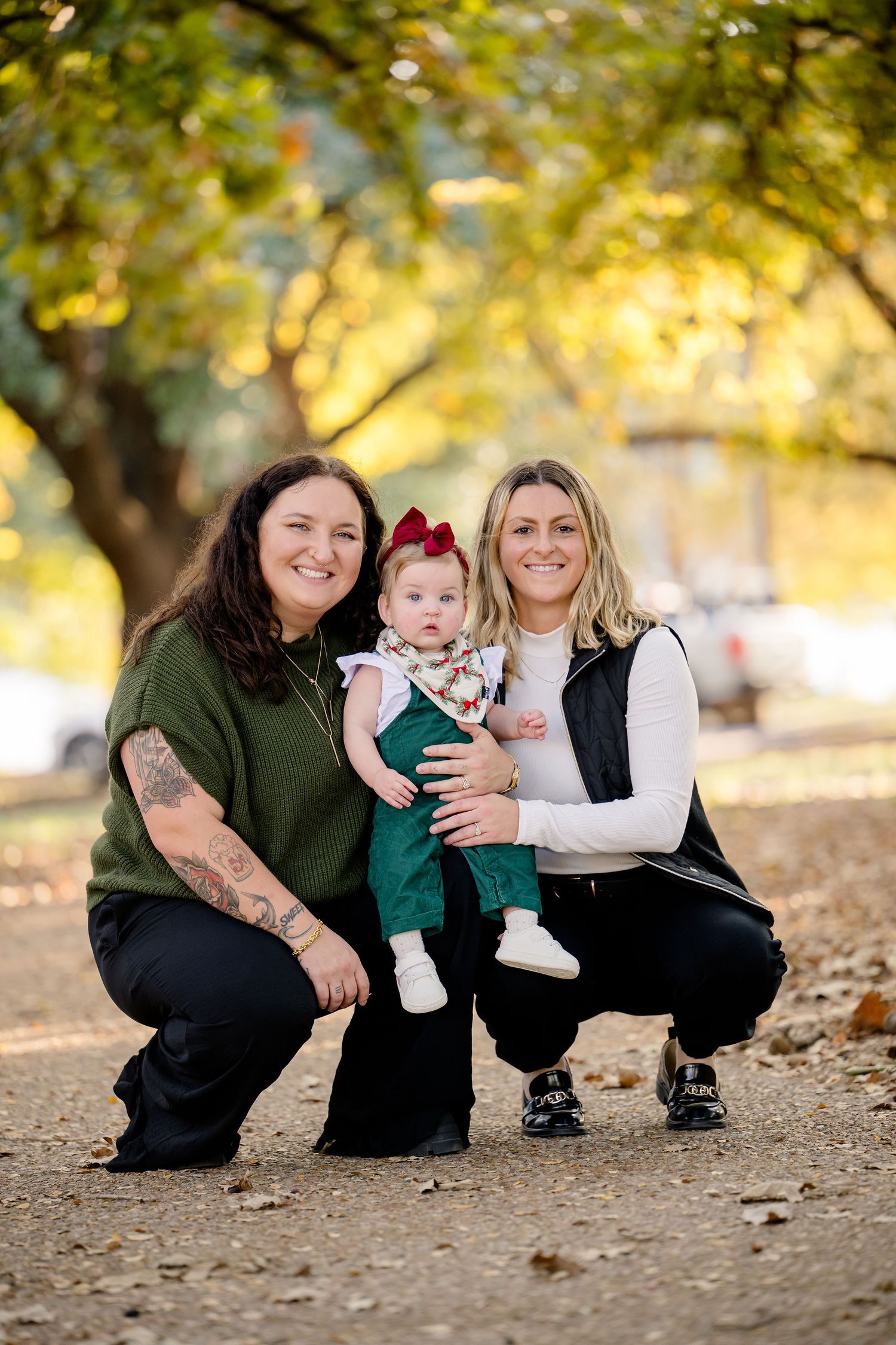 Family of three poses together on fallen autumn leaves in a park during golden hour sunset.