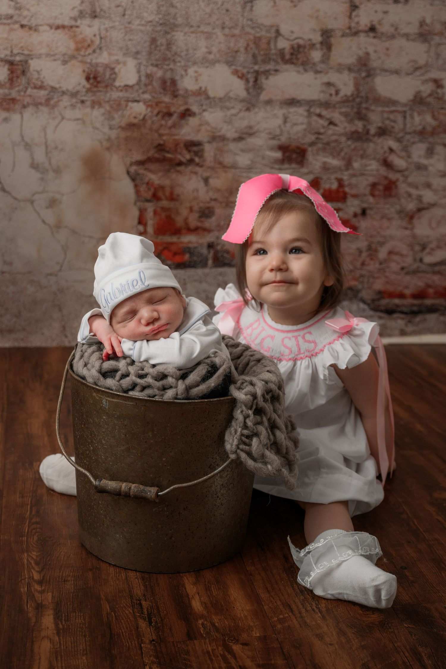 big sister sitting next to little brother posed in a bucket during his newborn photoshoot in Arlington Texas