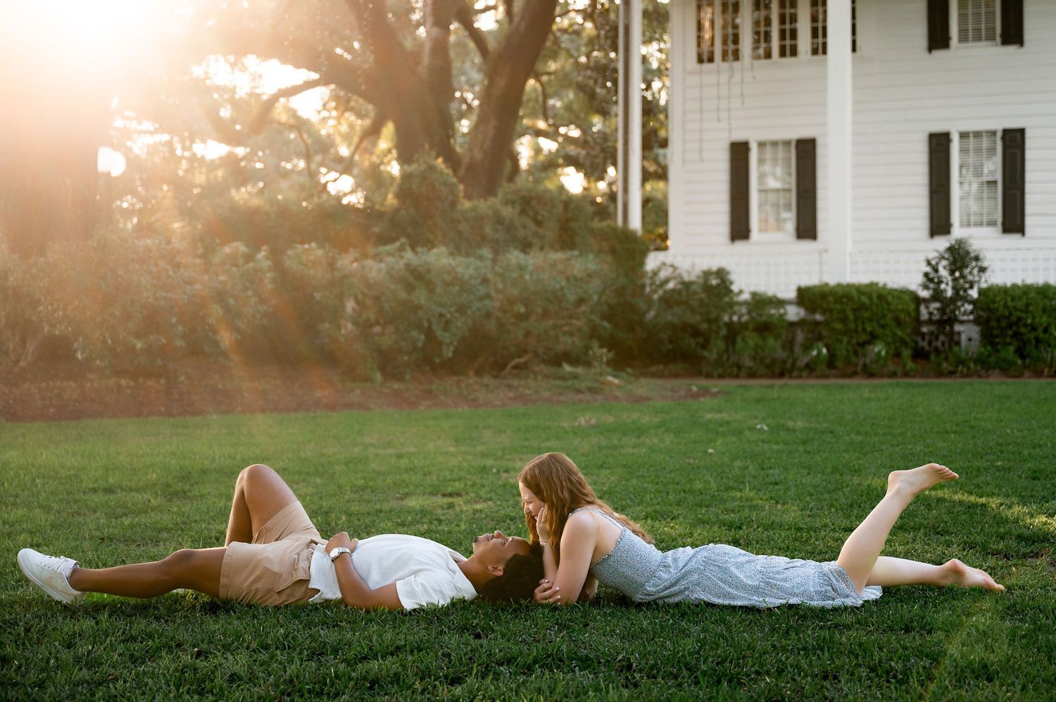 A romantic couple lying together on lush green grass during golden hour sunset.