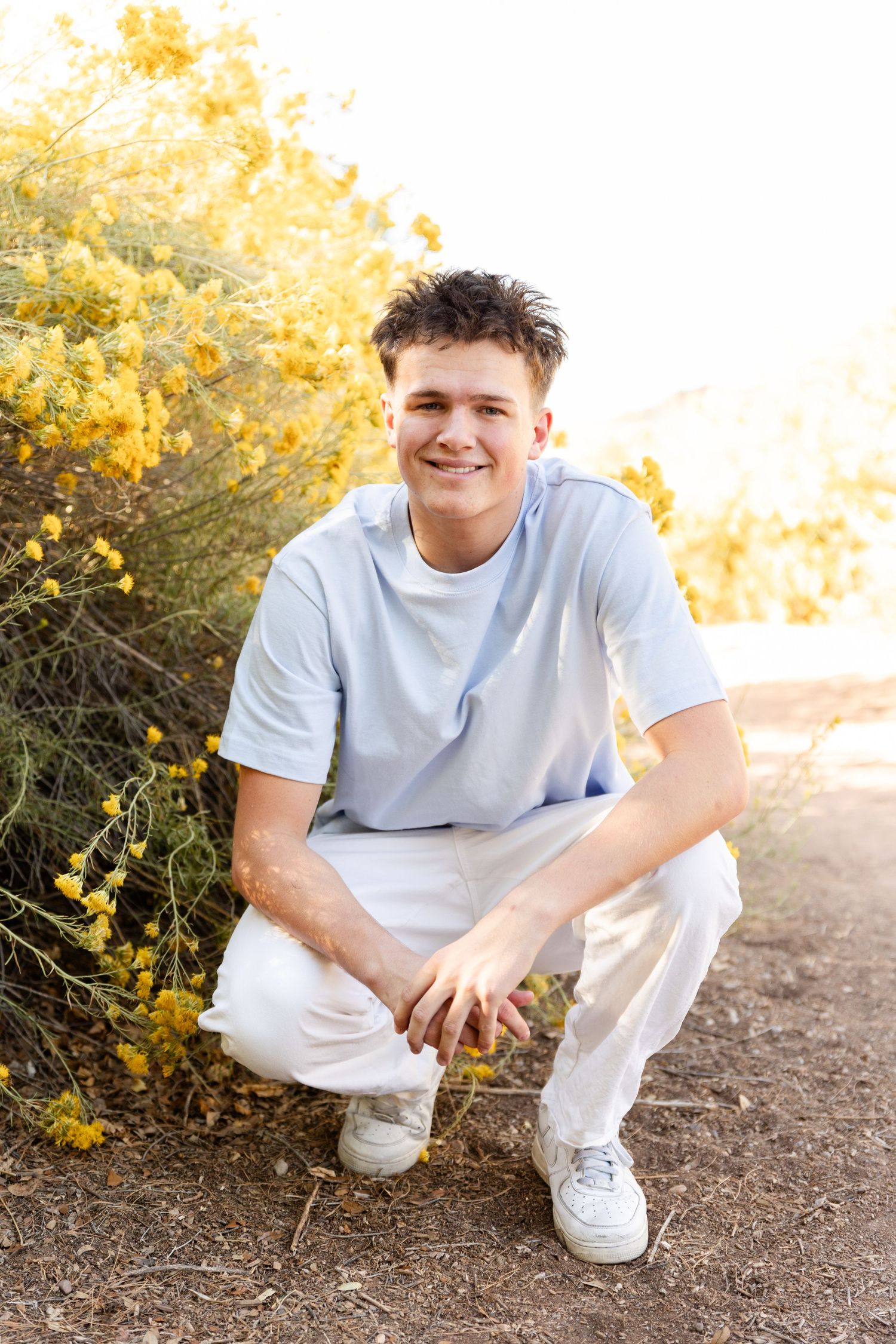 senior boy kneeling smiling at camera next to some bright yellow flowers a spring and fall statement in St. George utah