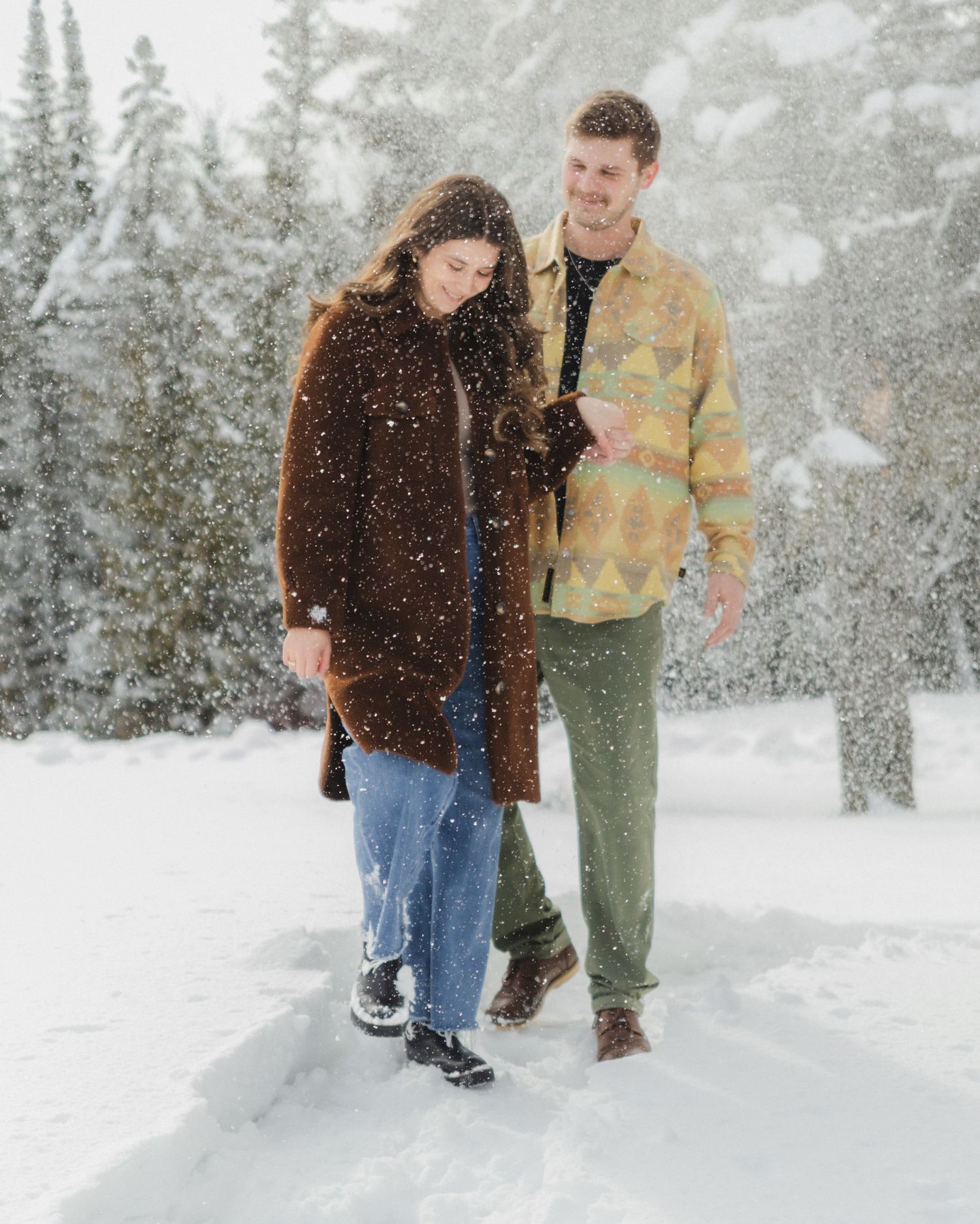 Two people walking together through a snowy forest landscape.