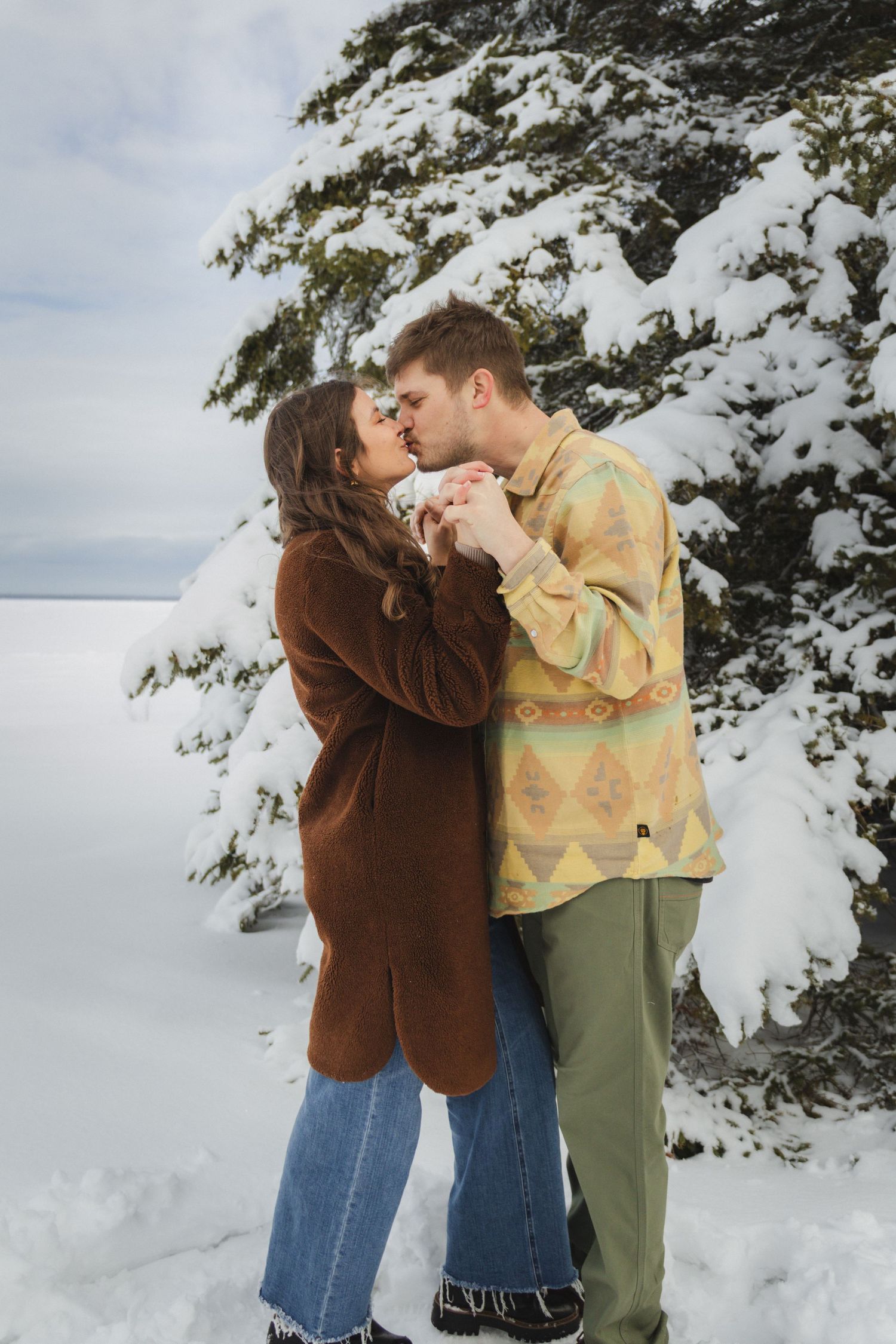 Romantic winter scene with couple embracing in snow-covered forest setting.