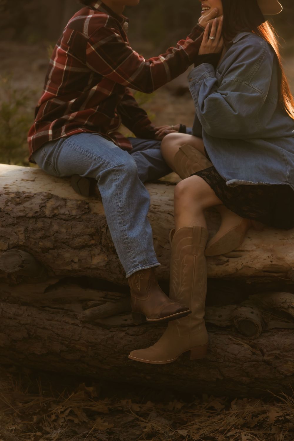 Two people in casual attire sit together on a fallen log in a rustic outdoor setting at sunset.