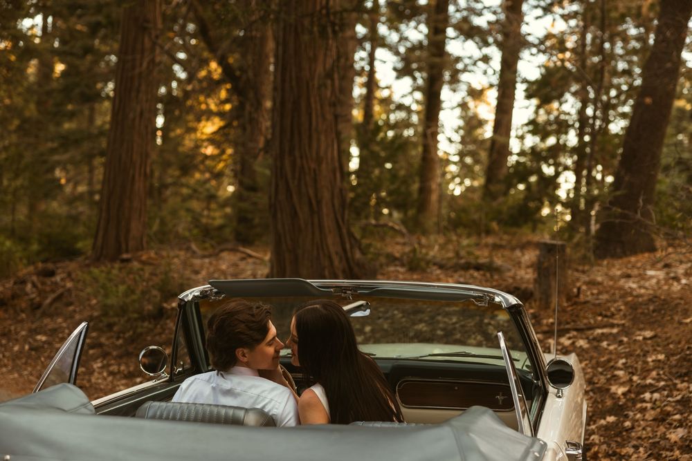 Classic convertible car parked in a scenic forest setting during golden hour sunset.