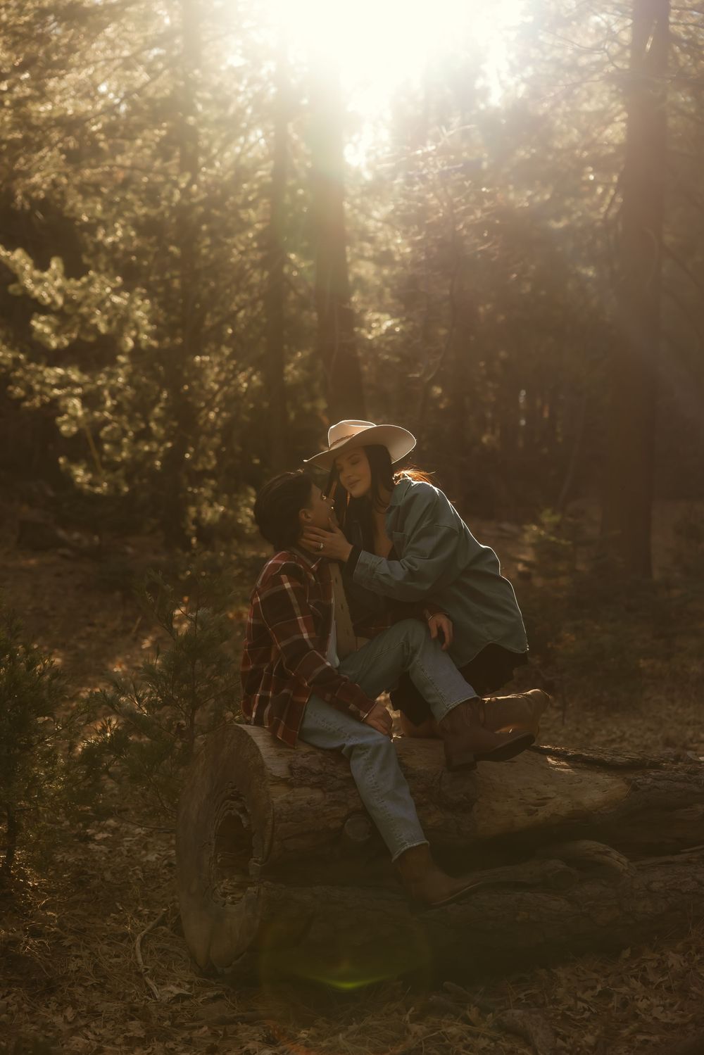 Two people sit together on fallen logs in a sunlit forest clearing as golden rays filter through the trees.
