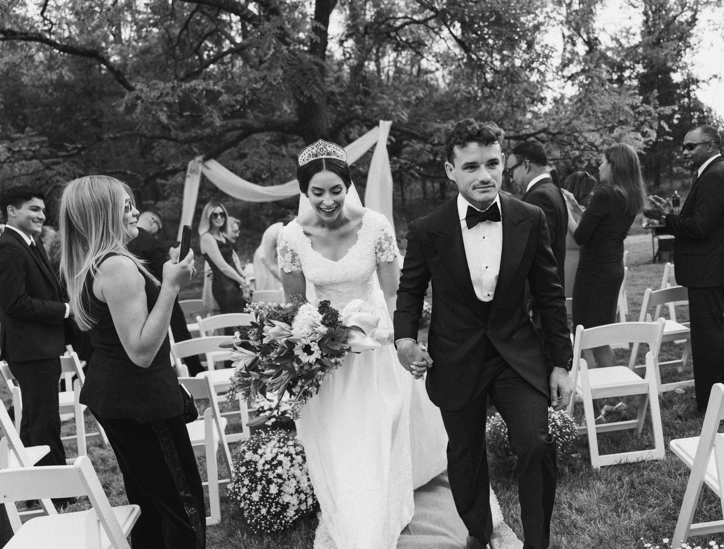 Wedding guests celebrate with joyful reactions during an outdoor ceremony.