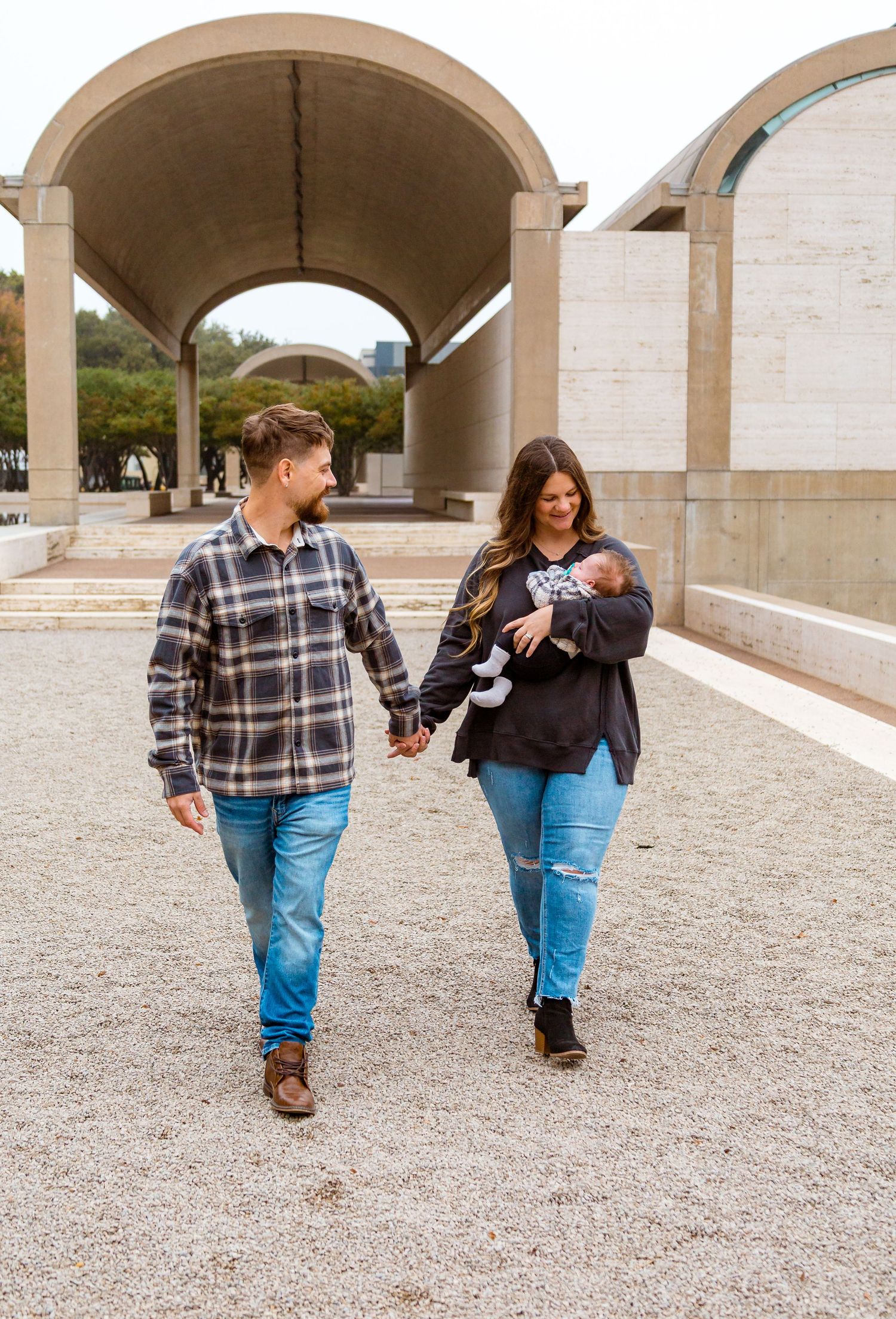 A couple walks together under concrete archways at a modern architectural site.