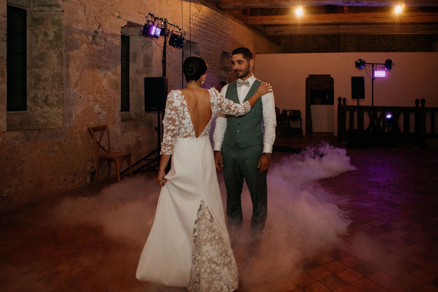 Bride and groom share their first dance surrounded by atmospheric fog on the dance floor in a stone venue.