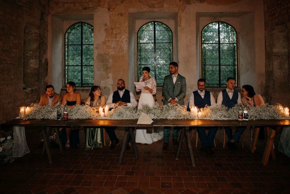 Wedding party seated at long candlelit table decorated with baby's breath in an elegant rustic stone venue.