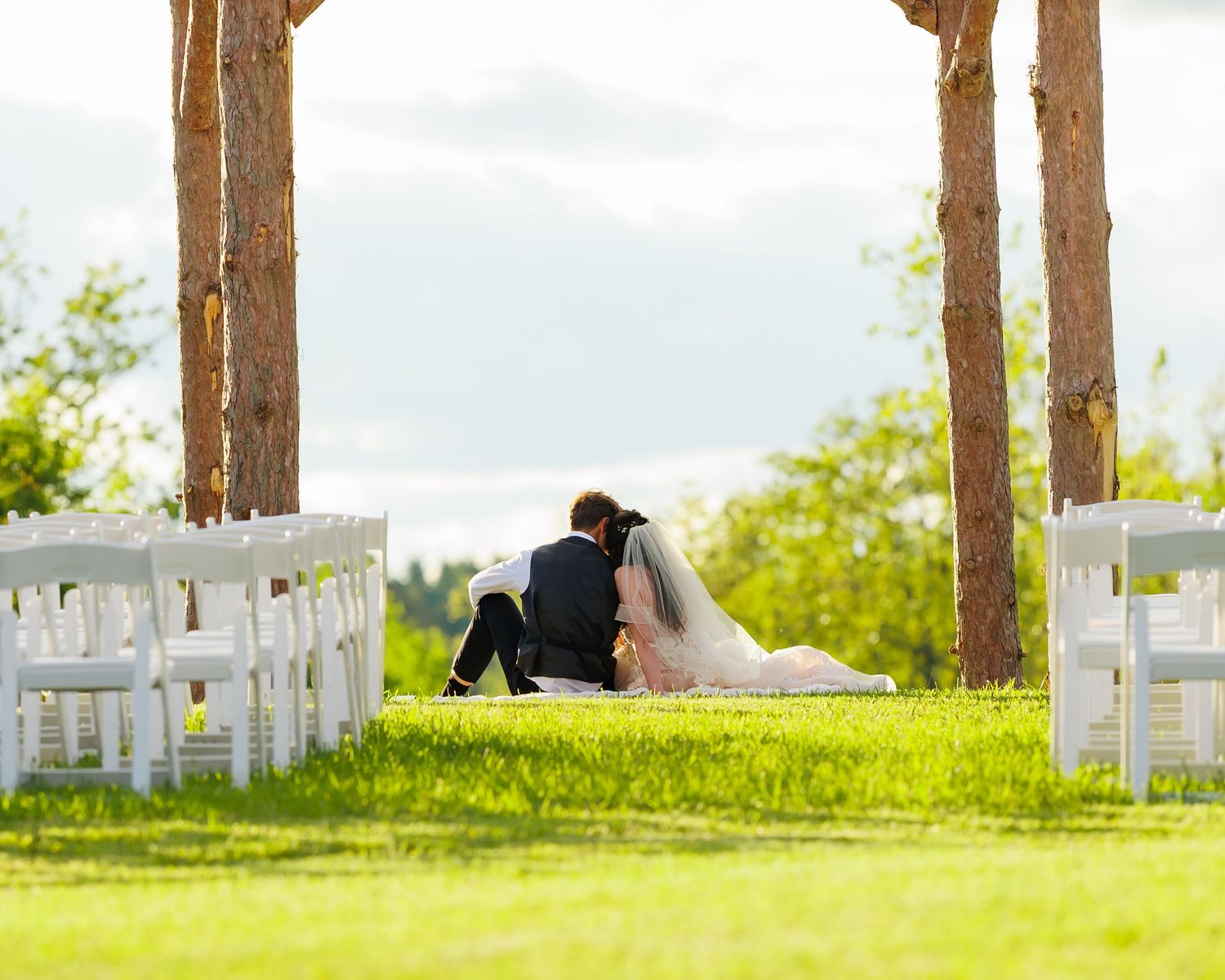 A bride and groom enjoy their time as newly-weds while watching the sun set under a wedding arbor.
