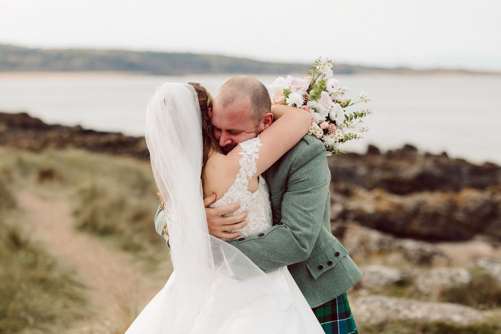 A tender embrace between newlyweds on a scenic coastal cliff overlooking the ocean.