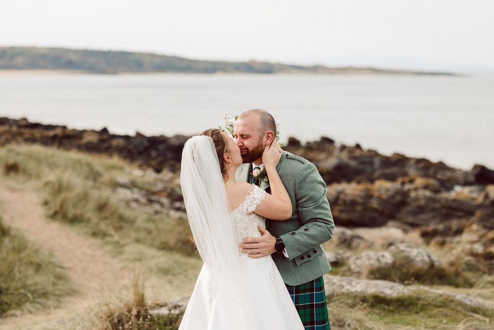 A couple shares an intimate moment along a scenic coastal path with rocky cliffs and ocean views.