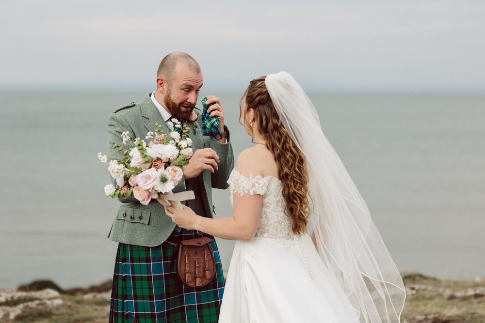 A romantic wedding moment captured against a misty coastal backdrop with dramatic cliffs and sea views.