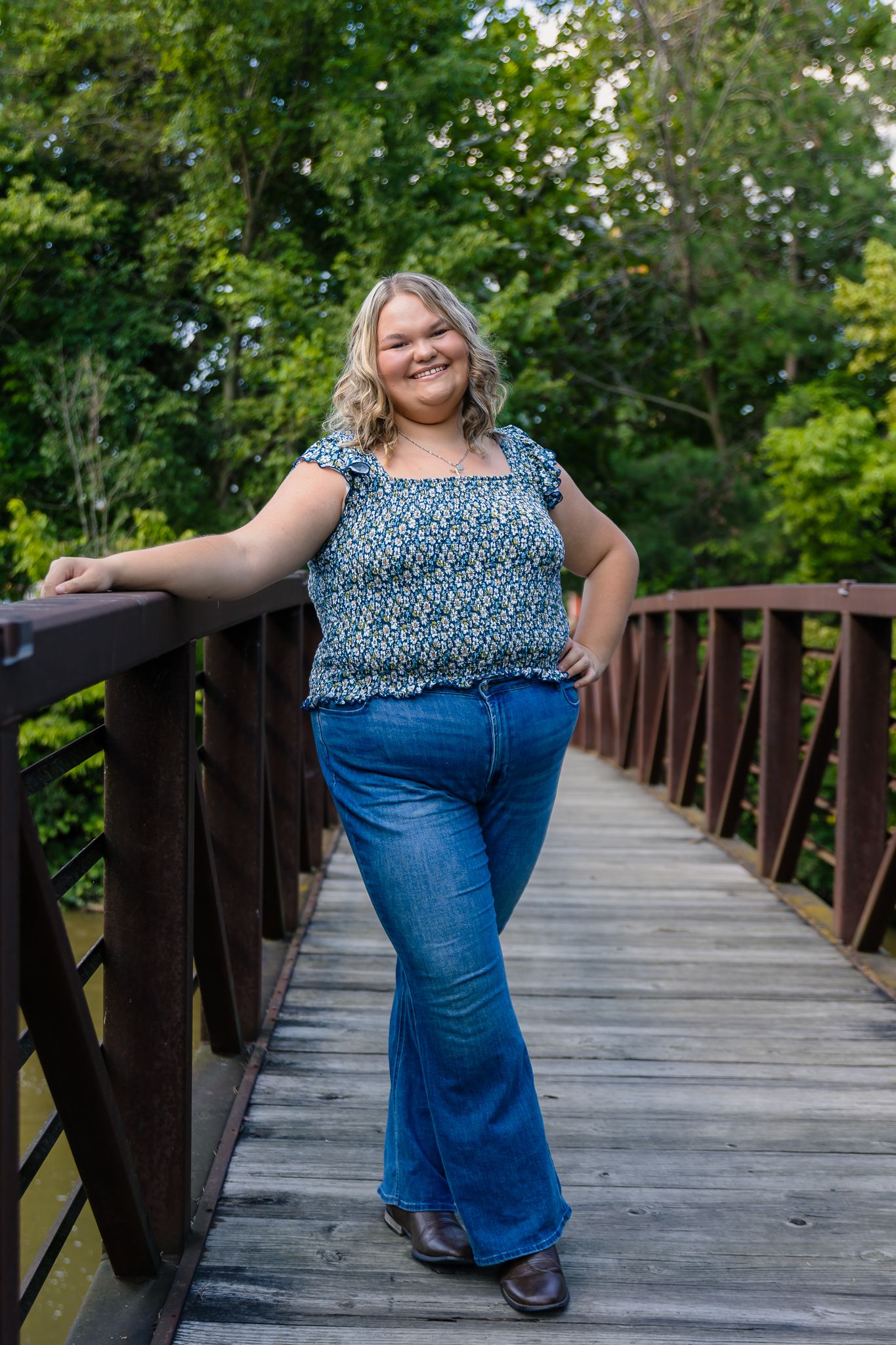 High school senior girl stands on bridge in Wilson Park in Milan, MI. She is smiling and posing for a senior photo.