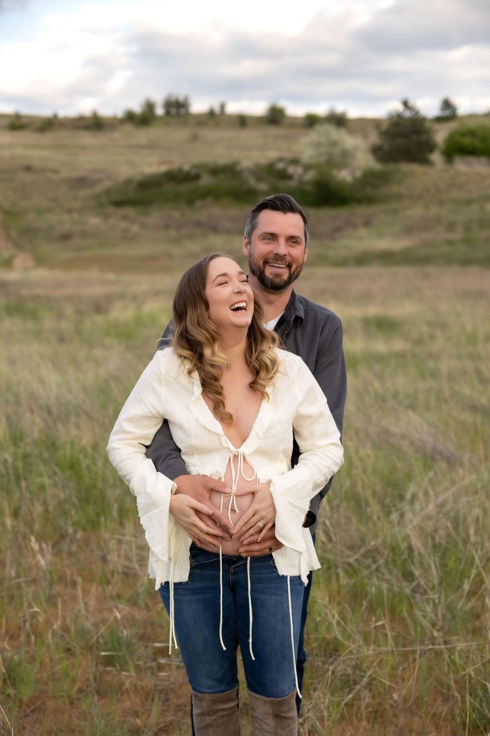 A couple shares a joyful moment together in a grassy field during a maternity photo session.
