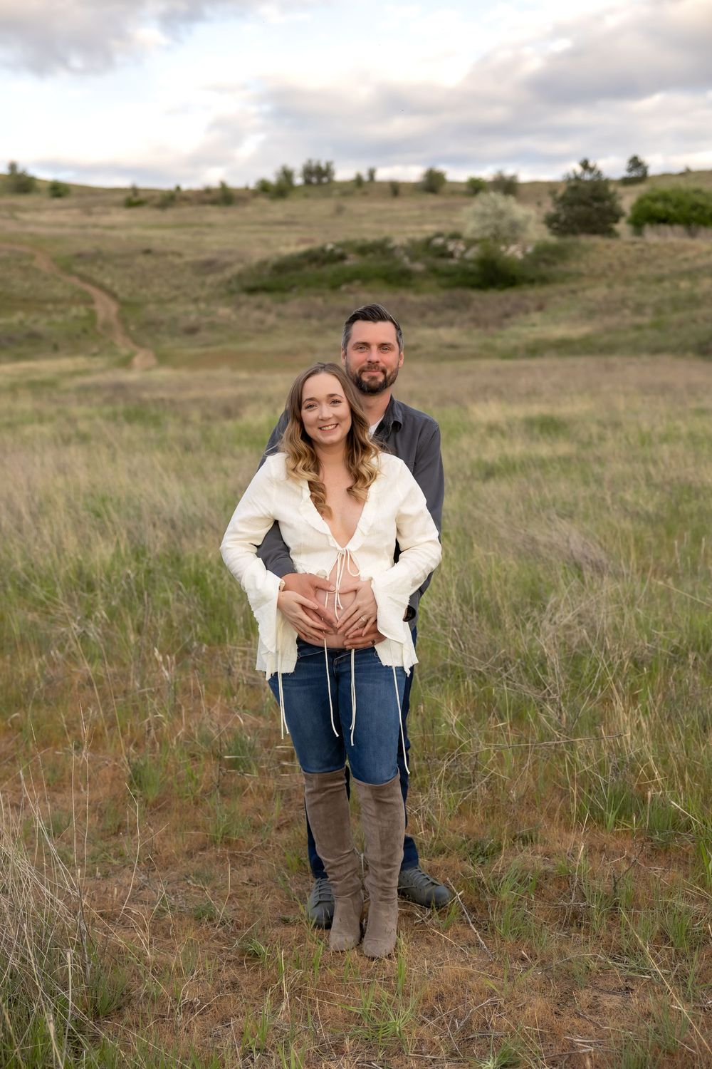 Maternity photoshoot in a rustic field setting with rolling hills in the background.