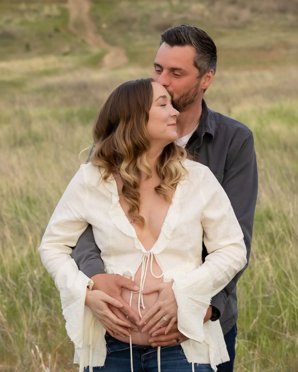 A couple shares an intimate moment in a grassy field, with the person in white wearing a bell-sleeved top.