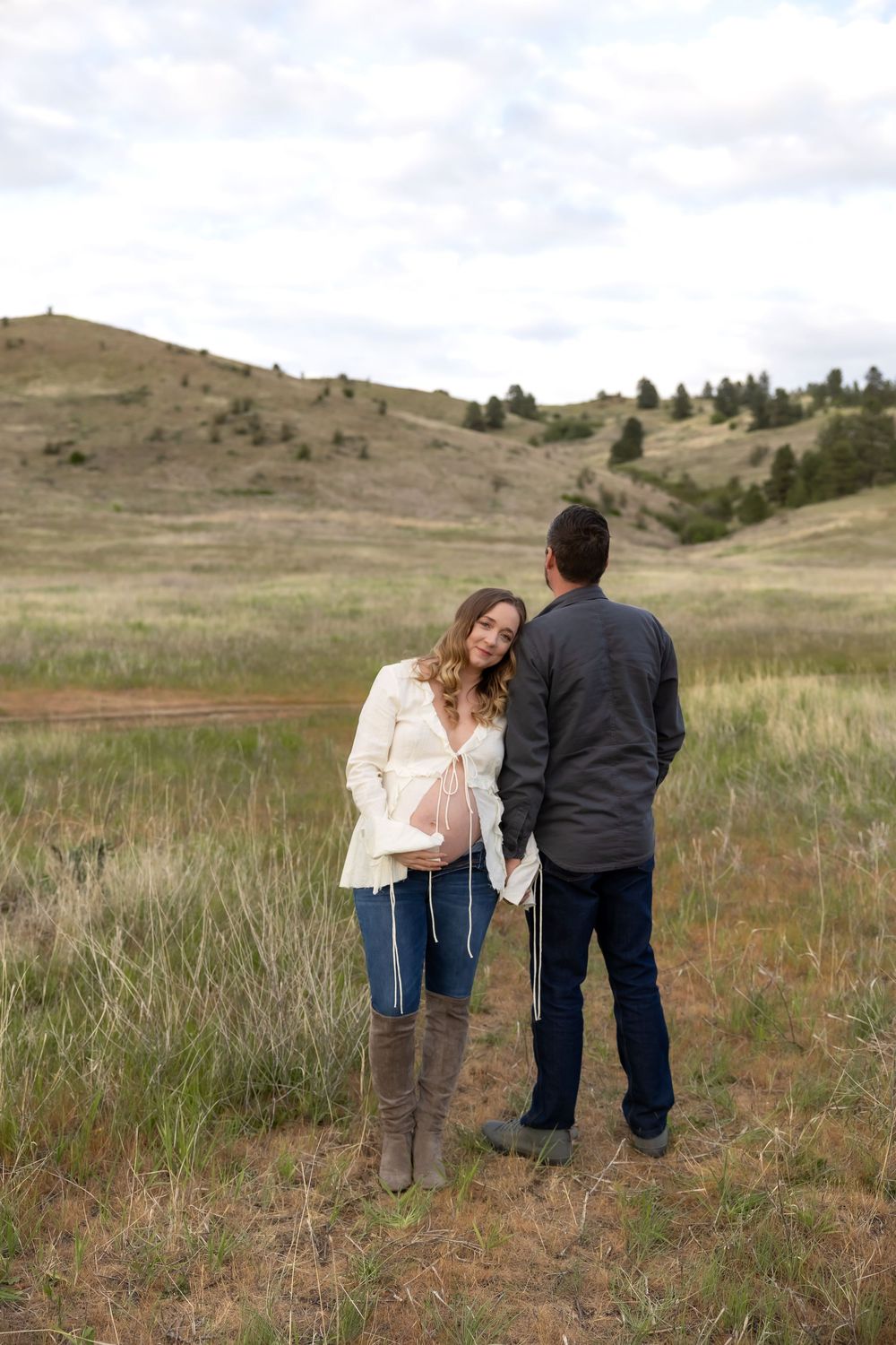 A couple shares a romantic moment in a scenic mountain meadow with rolling hills and grass in the background.