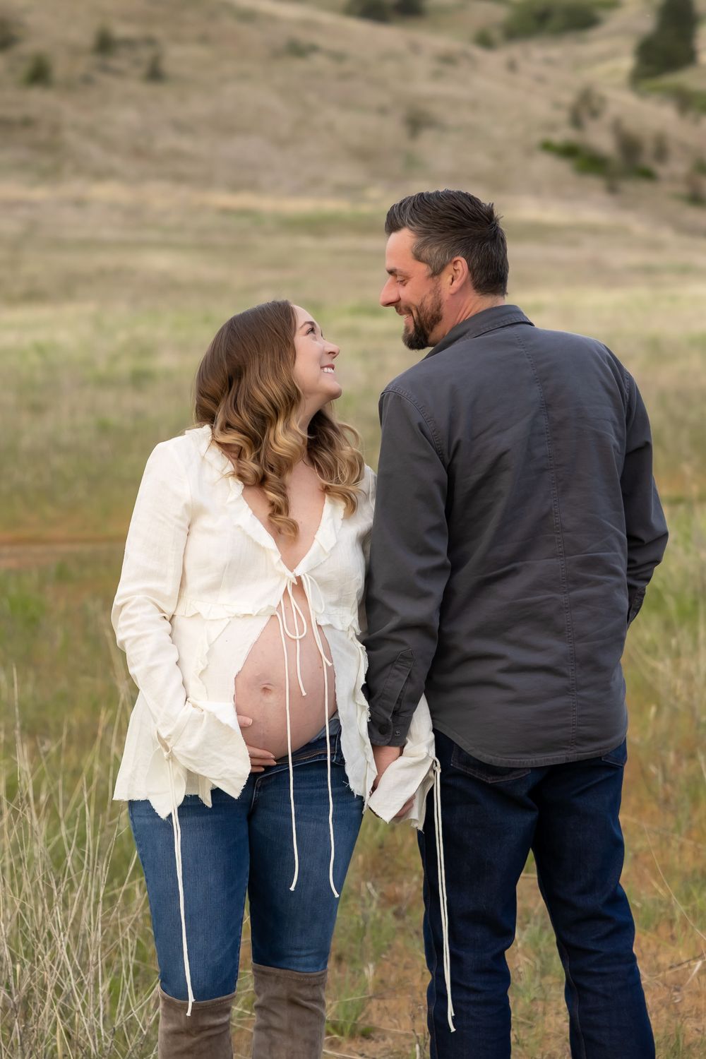 Two people share a tender moment while standing in a scenic mountain meadow at golden hour.