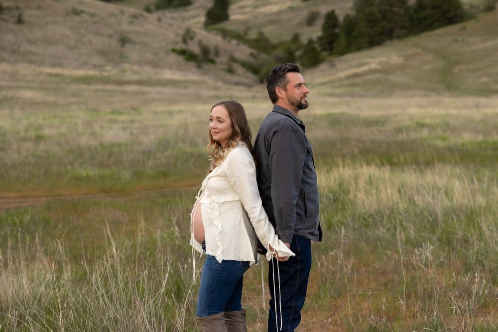 A romantic moment captured in a natural meadow setting with rolling hills in the background.