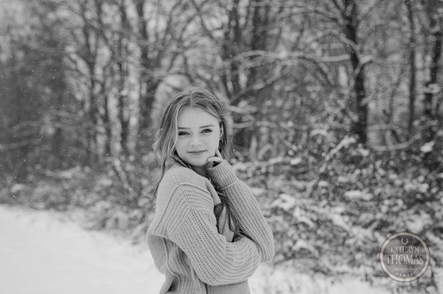 Black and white winter portrait with a chunky knit sweater against a snowy forest setting.