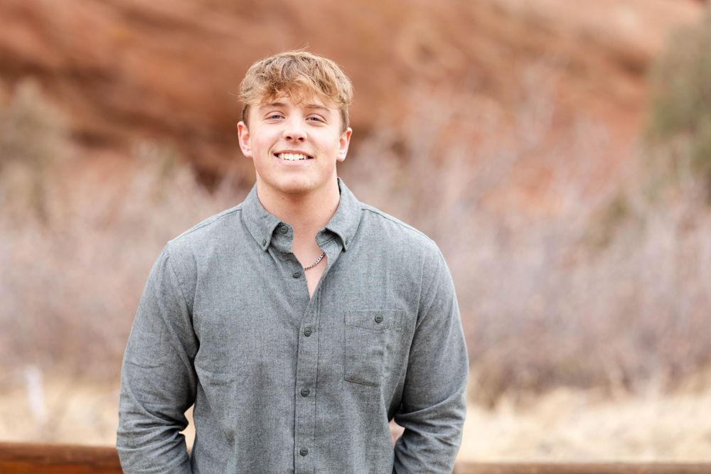 Portrait of person in grey button-down shirt with desert rocks in background.