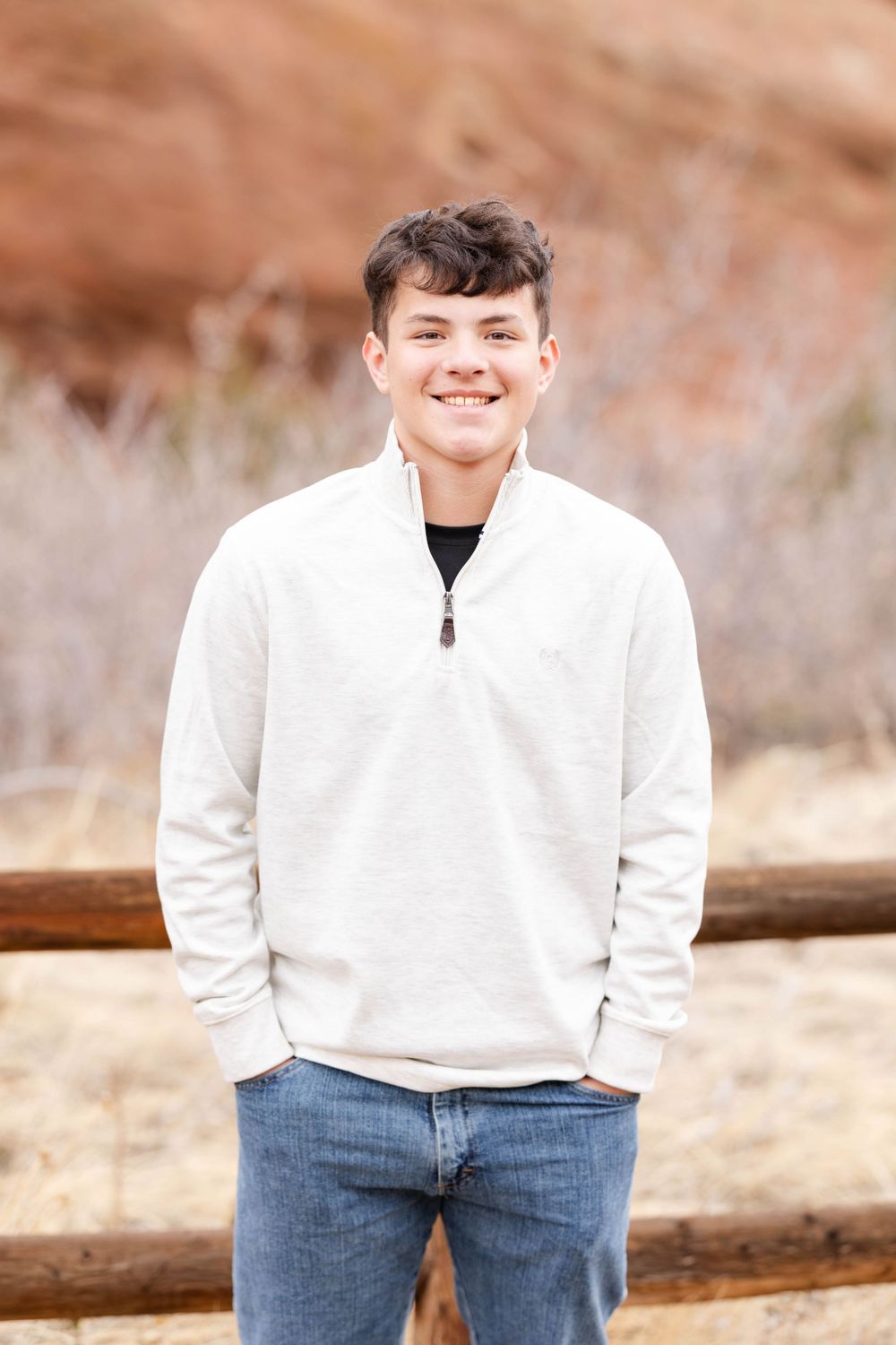 Person in white quarter-zip sweater and jeans poses against desert landscape.