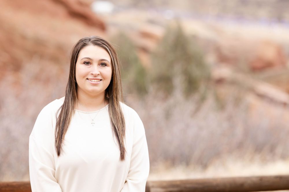 Portrait of person in cream colored sweater with red rocks in background.