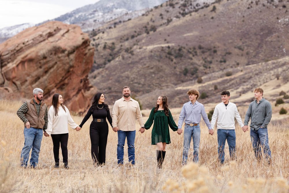 Group holds hands in line formation against backdrop of desert mountains and red rocks.