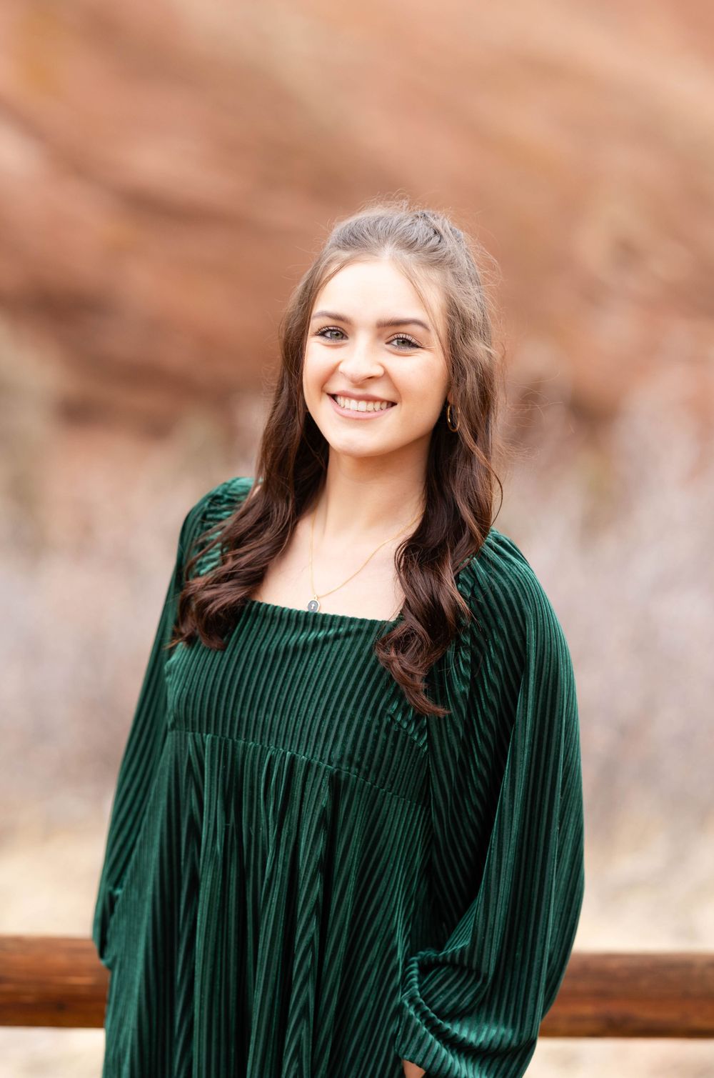 Portrait of person in emerald green dress against rustic desert backdrop.