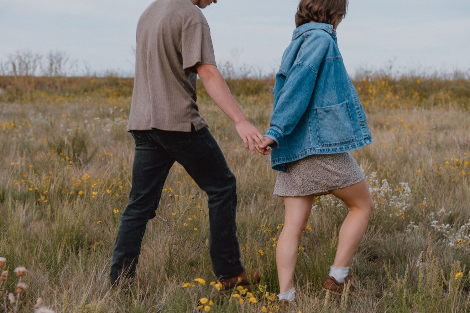 Two people walking together holding hands in a wildflower field with casual clothing.
