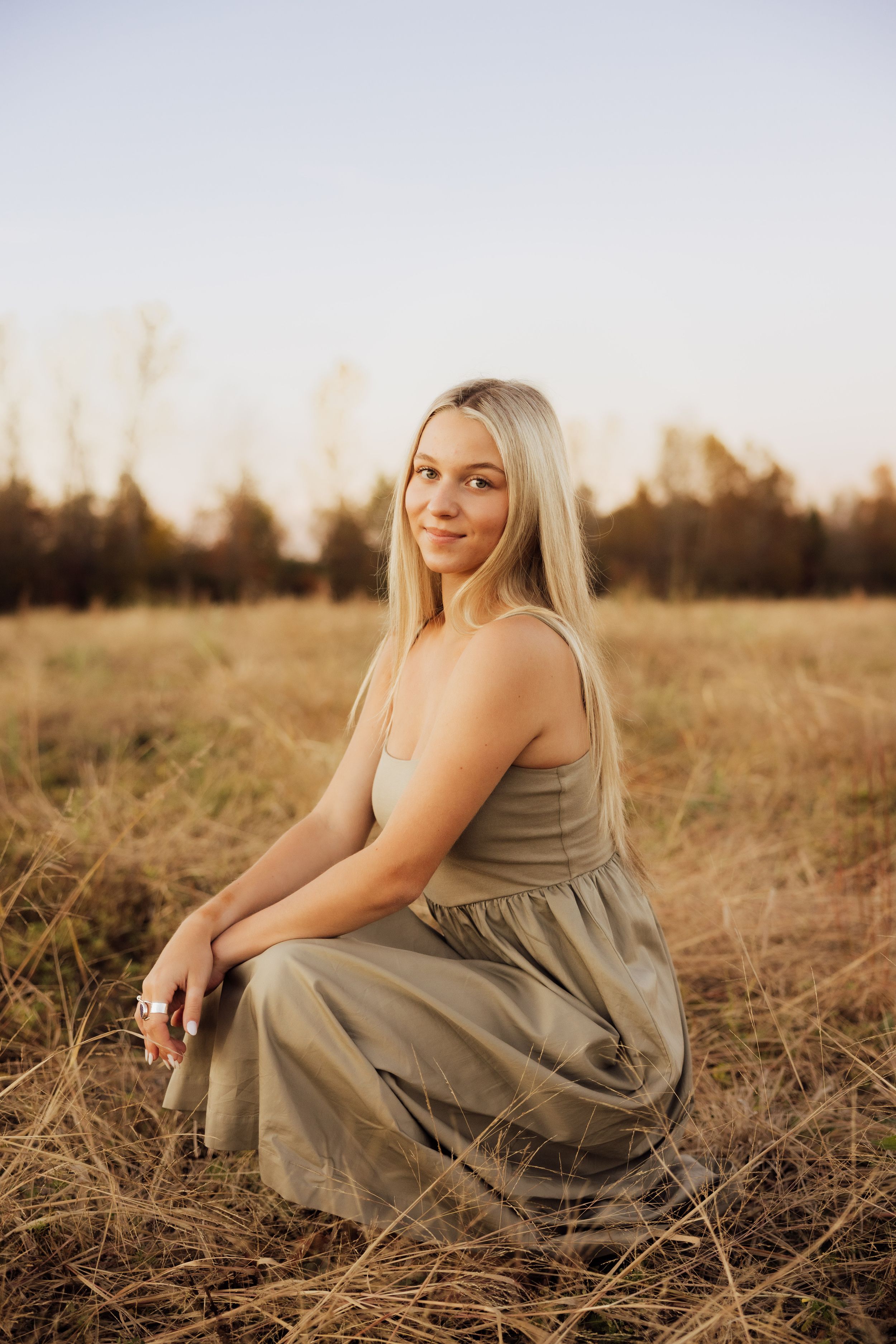 Senior sunset portrait session in a rustic field with golden hour lighting.