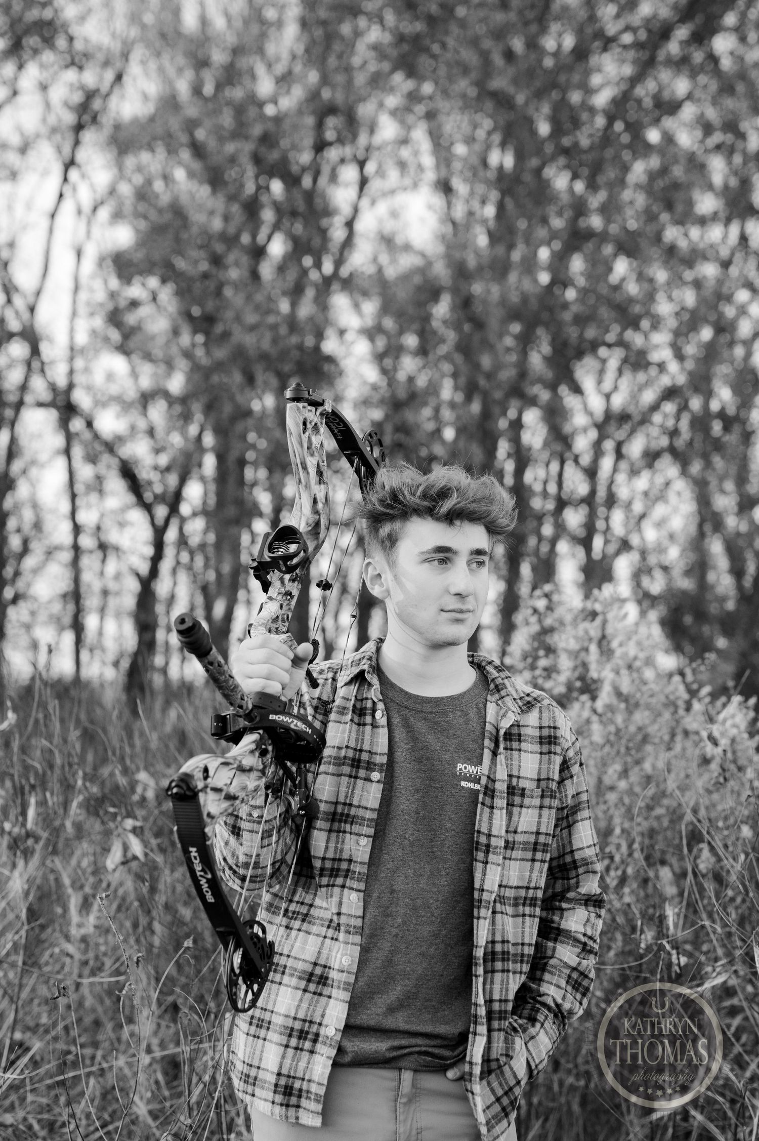 Monochrome portrait of archer with modern compound bow against forest backdrop.