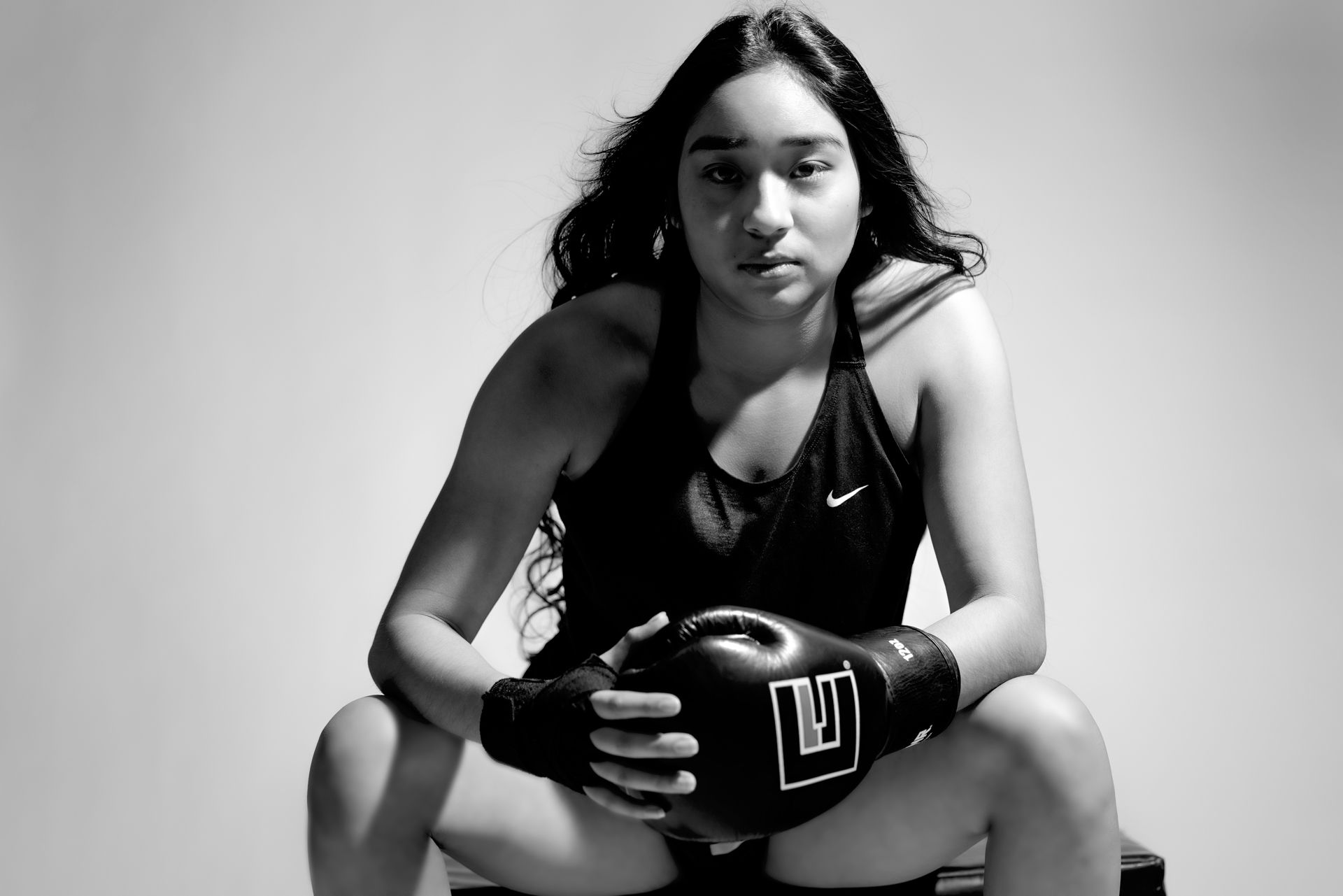 Black and white sports portrait of an athlete squatting in Nike gear with boxing gloves against neutral background.
