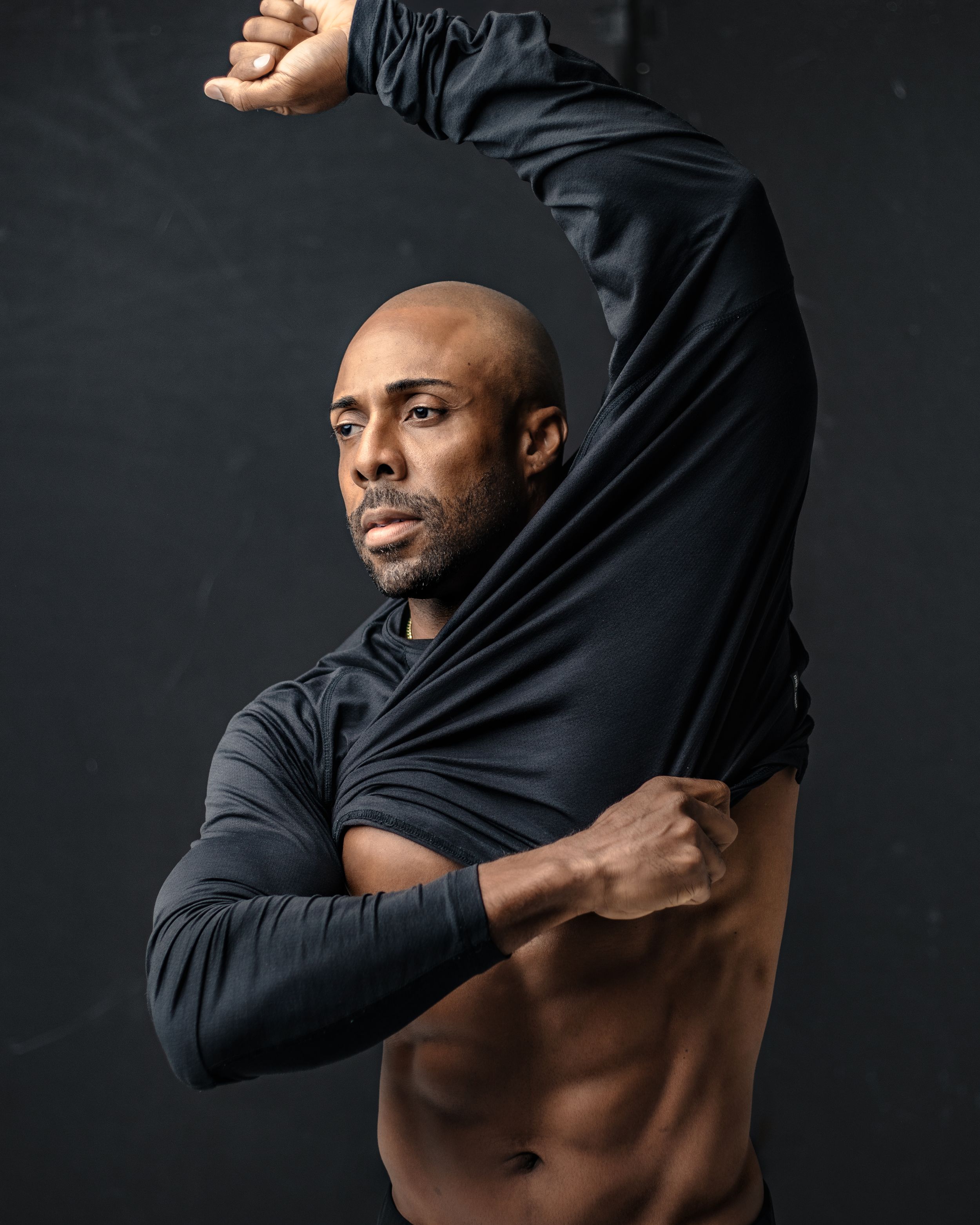 Athletic man in black clothing showing muscular physique against dark background. Male model.