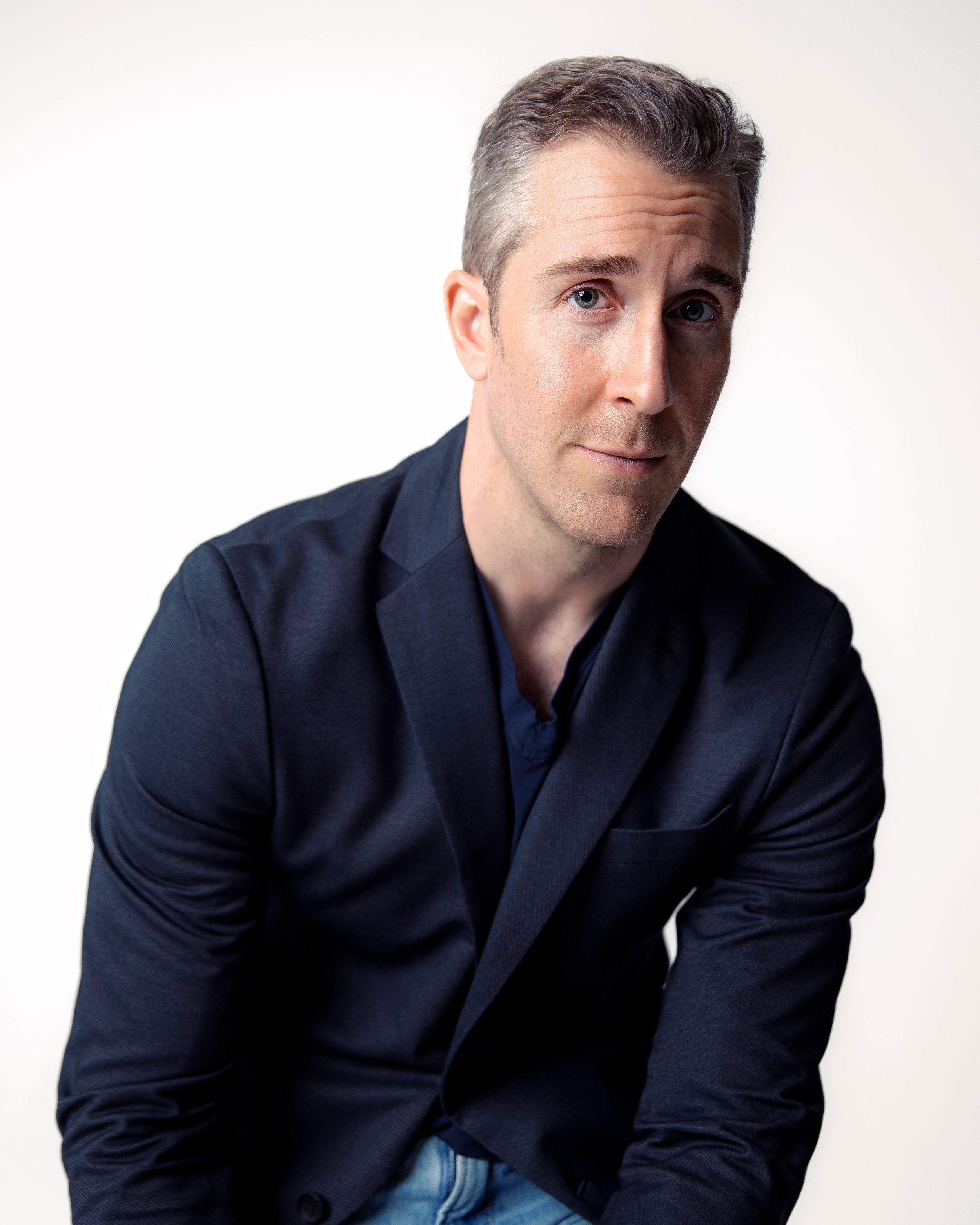 Professional headshot of man in navy blazer against white background.