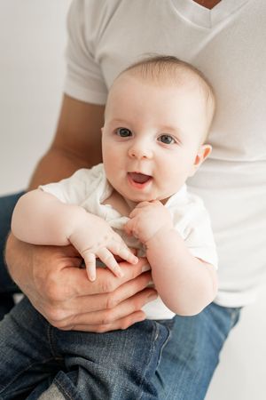 A series of photos showing a baby in a white onesie being held by someone wearing a white shirt and jeans.