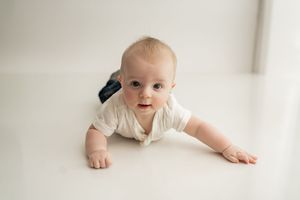 Close up portrait style image showing a young baby in a soft white studio setting against light backgrounds.
