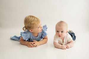 Two young children lying on a white background wearing blue and beige outfits.