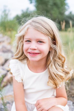 A series of photos showing a child with blonde hair in a white dress smiling and laughing outdoors.