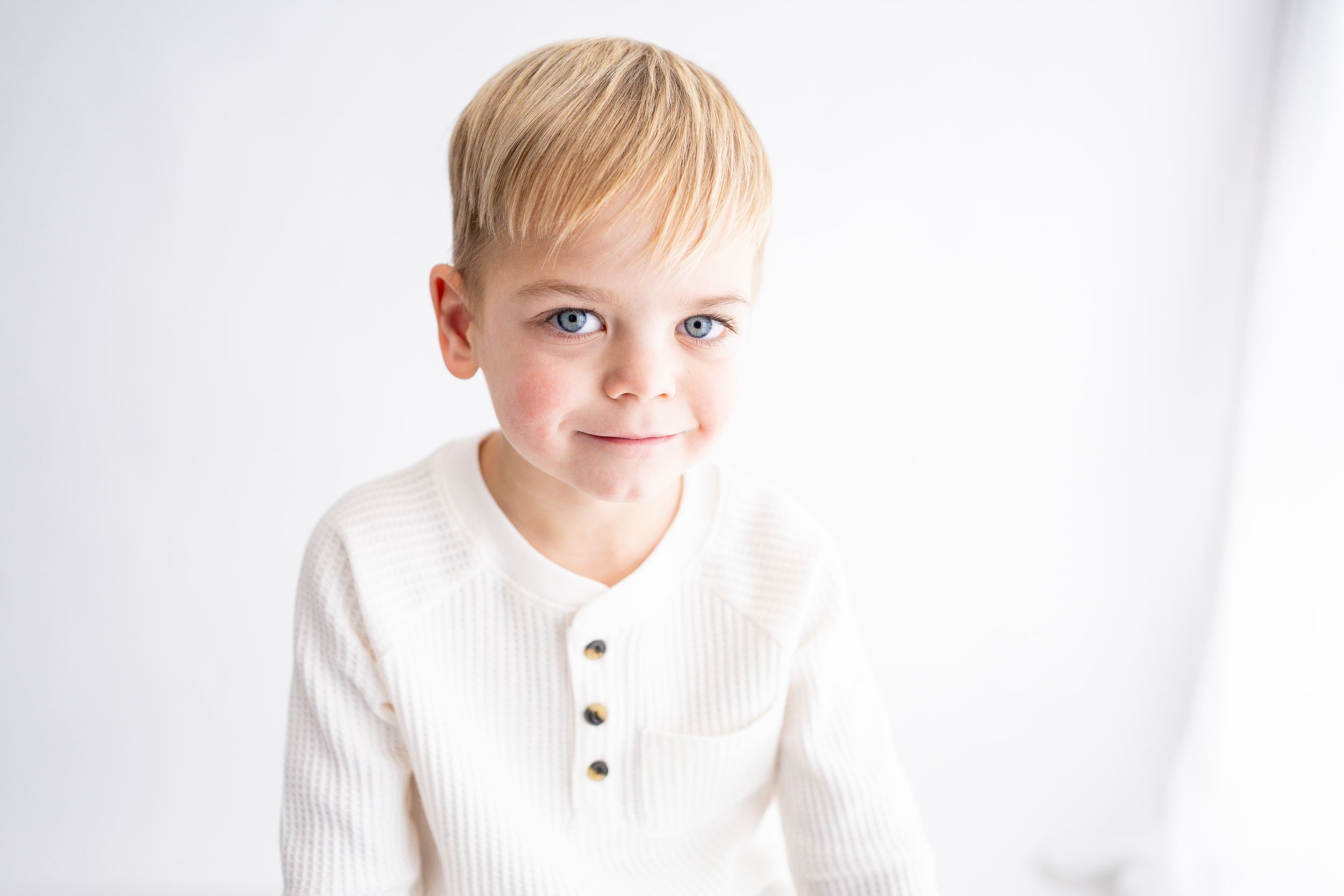 A small child in a white ribbed sweater poses against a bright white background.