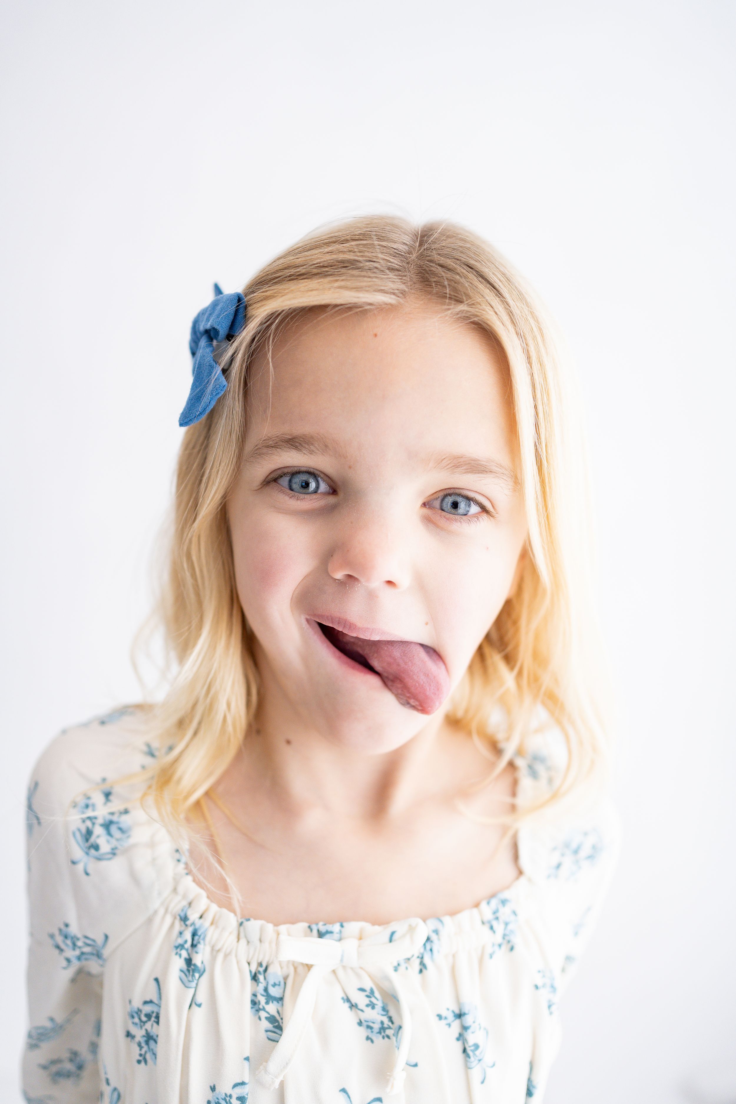 A playful child in a white and blue floral dress sticks out their tongue while posing for three sequential photos.