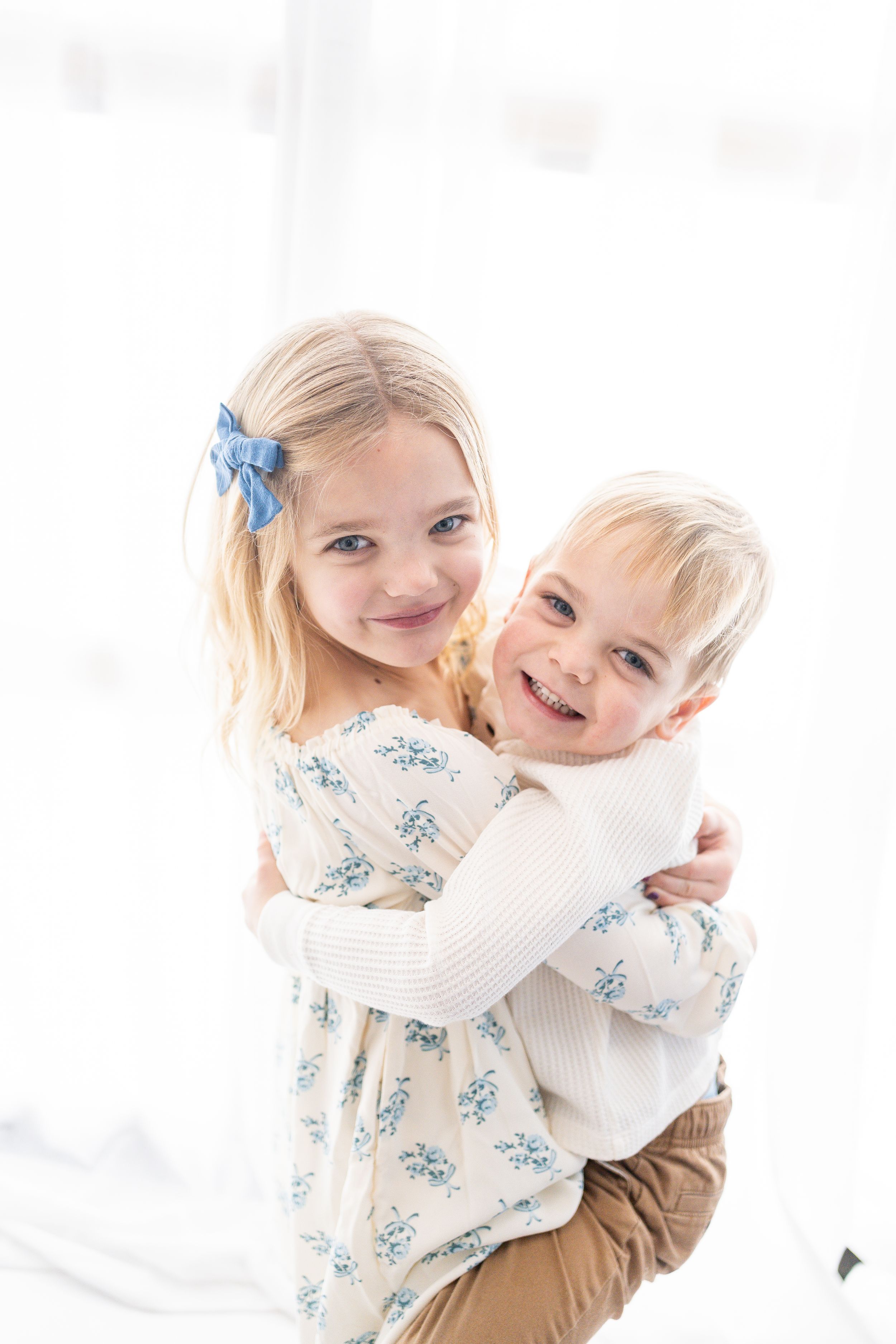 Two young children in white and blue outfits playing and laughing together in a bright studio setting.