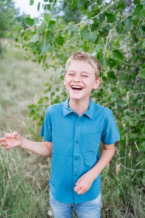 Three candid photos show someone wearing a blue polo shirt and jeans laughing joyfully outdoors near green foliage.