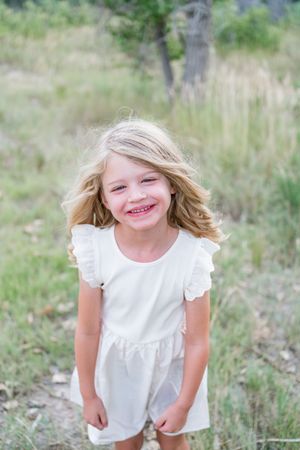 Young child in white dress plays outdoors in a grassy field on a sunny day.