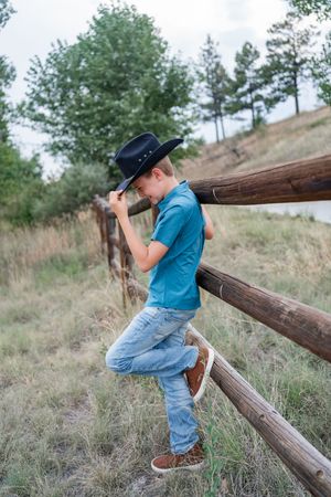 Four sequential images show a young child in blue and denim playing on rustic wooden fence posts in a grassy field.