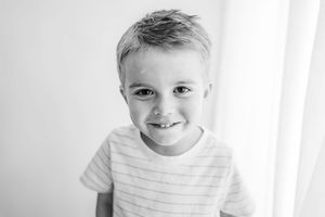 Child in striped shirt smiling brightly in black and white portrait.